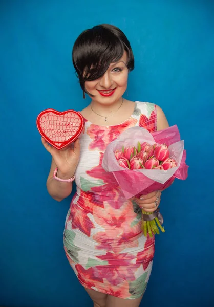 Bahar elbise sevimli gülümseyen kız stüdyoda mavi bir arka plan üzerinde tulip buket pembe taze tutar. o gerçekten hediye ve kesinlikle mutlu bulunuyor.