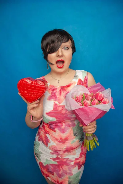 Bahar elbise sevimli gülümseyen kız stüdyoda mavi bir arka plan üzerinde tulip buket pembe taze tutar. o gerçekten hediye ve kesinlikle mutlu bulunuyor.