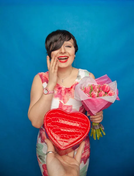 Bahar elbise sevimli gülümseyen kız stüdyoda mavi bir arka plan üzerinde tulip buket pembe taze tutar. o gerçekten hediye ve kesinlikle mutlu bulunuyor.