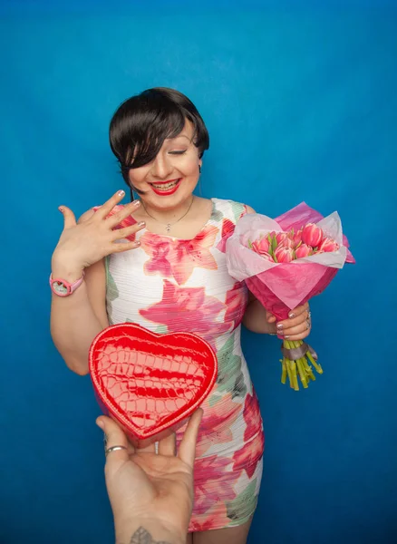 Bahar elbise sevimli gülümseyen kız stüdyoda mavi bir arka plan üzerinde tulip buket pembe taze tutar. o gerçekten hediye ve kesinlikle mutlu bulunuyor.