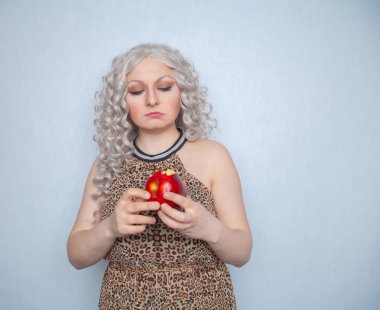 Yazlık elbise giyen ve beyaz arka planda yalnız büyük kırmızı elma ile poz tombul sarışın kız 