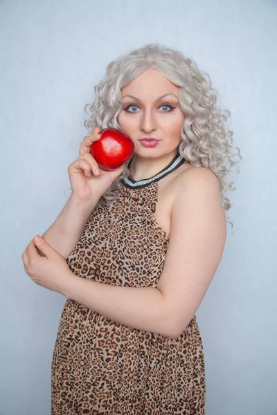 chubby blonde girl wearing summer dress and posing with big red apple on white background alone