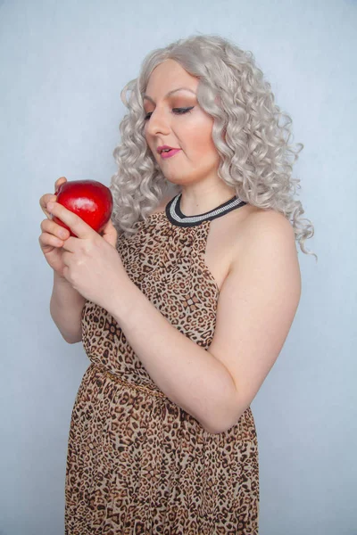 chubby blonde girl wearing summer dress and posing with big red apple on white background alone