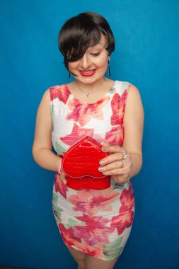 Mavi stüdyo düz arka plan üzerinde kırmızı kalp şekli hediye kutusu ile oldukça mutlu esmer