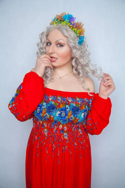cute chubby girl with flowers in white curly hair in red rustic dress