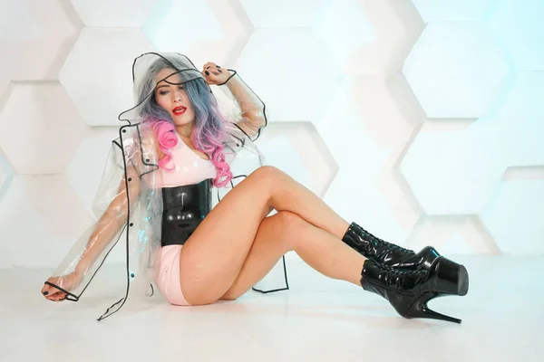 tanned woman in latex clothes and transparent futuristic raincoat on white Studio background