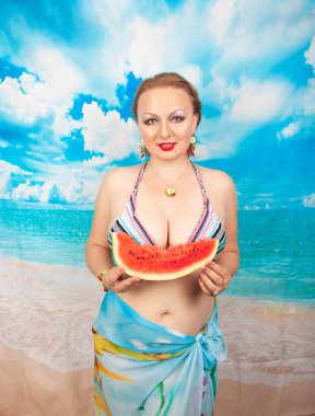 sevimli tombul sarışın bir mayo büyük göğüsler ile karpuz bir parça ile standları ve yemek ve dinlenme sahiptir