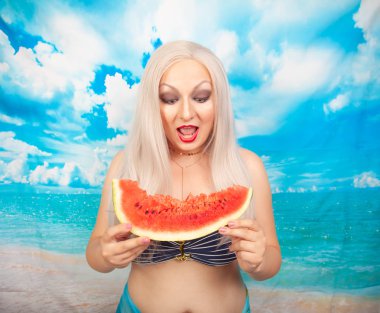 sevimli tombul sarışın bir mayo büyük göğüsler ile karpuz bir parça ile standları ve yemek ve dinlenme sahiptir