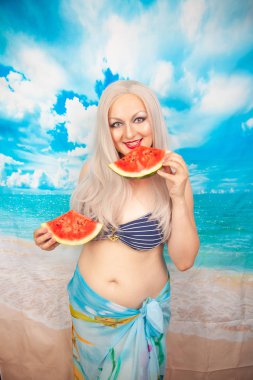 sevimli tombul sarışın bir mayo büyük göğüsler ile karpuz bir parça ile standları ve yemek ve dinlenme sahiptir