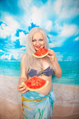 sevimli tombul sarışın bir mayo büyük göğüsler ile karpuz bir parça ile standları ve yemek ve dinlenme sahiptir