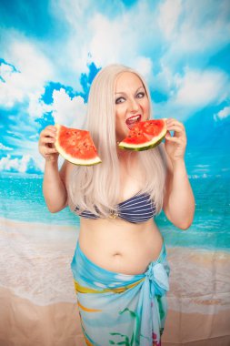 sevimli tombul sarışın bir mayo büyük göğüsler ile karpuz bir parça ile standları ve yemek ve dinlenme sahiptir