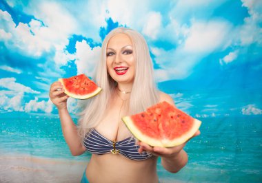 sevimli tombul sarışın bir mayo büyük göğüsler ile karpuz bir parça ile standları ve yemek ve dinlenme sahiptir