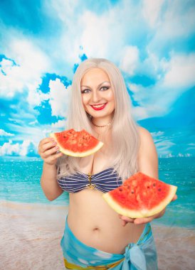 sevimli tombul sarışın bir mayo büyük göğüsler ile karpuz bir parça ile standları ve yemek ve dinlenme sahiptir