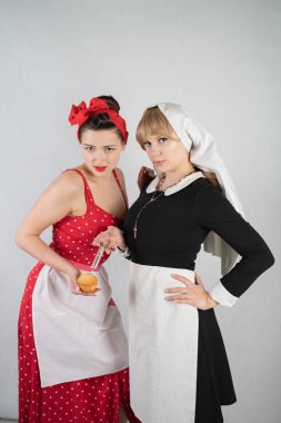 iki sevimli kız arkadaşım için bir kostüm cosplay parti giyinmiş. bir kız pinup tarzı bir ev hanımı olarak giyinmiş, ikinci kadın bir rahibe olarak bir şırınga ile giyinmiş. Beyaz bir arka plan üzerinde duruyorlar.