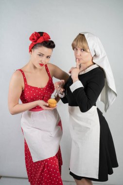 iki sevimli kız arkadaşım için bir kostüm cosplay parti giyinmiş. bir kız pinup tarzı bir ev hanımı olarak giyinmiş, ikinci kadın bir rahibe olarak bir şırınga ile giyinmiş. Beyaz bir arka plan üzerinde duruyorlar.