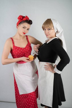 iki sevimli kız arkadaşım için bir kostüm cosplay parti giyinmiş. bir kız pinup tarzı bir ev hanımı olarak giyinmiş, ikinci kadın bir rahibe olarak bir şırınga ile giyinmiş. Beyaz bir arka plan üzerinde duruyorlar.