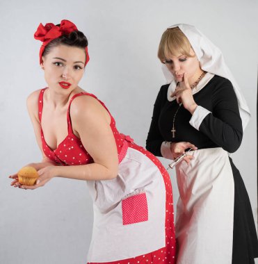 iki sevimli kız arkadaşım için bir kostüm cosplay parti giyinmiş. bir kız pinup tarzı bir ev hanımı olarak giyinmiş, ikinci kadın bir rahibe olarak bir şırınga ile giyinmiş. Beyaz bir arka plan üzerinde duruyorlar.