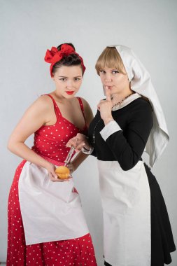 iki sevimli kız arkadaşım için bir kostüm cosplay parti giyinmiş. bir kız pinup tarzı bir ev hanımı olarak giyinmiş, ikinci kadın bir rahibe olarak bir şırınga ile giyinmiş. Beyaz bir arka plan üzerinde duruyorlar.