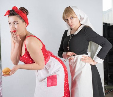 iki sevimli kız arkadaşım için bir kostüm cosplay parti giyinmiş. bir kız pinup tarzı bir ev hanımı olarak giyinmiş, ikinci kadın bir rahibe olarak bir şırınga ile giyinmiş. Beyaz bir arka plan üzerinde duruyorlar.
