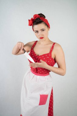 Kız ev kadını kırmızı vintage puantiyeli elbise kadar tehlikeli PIN onun elinde büyük bir bıçak ile duruyor ve öfkeyle beyaz katı studio özgeçmişlerine sevinir