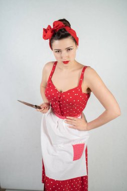 Kız ev kadını kırmızı vintage puantiyeli elbise kadar tehlikeli PIN onun elinde büyük bir bıçak ile duruyor ve öfkeyle beyaz katı studio özgeçmişlerine sevinir