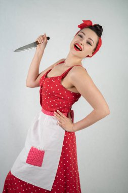 Kız ev kadını kırmızı vintage puantiyeli elbise kadar tehlikeli PIN onun elinde büyük bir bıçak ile duruyor ve öfkeyle beyaz katı studio özgeçmişlerine sevinir