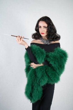 siyah gece elbisesi kız ve onun elinde bir yeşil tüylü boa büyüleyici zarif pin duruyor ve beyaz katı Studio zemin üzerinde bir ağızlık ile bir sigara içiyor