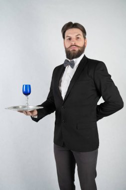 elini ve bir kadeh şarap beyaz sağlam bir arka plan stüdyo üzerinde çelik bir tepsi ile resmi iş takım elbiseli sakallı beyaz hizmetçi duruyor