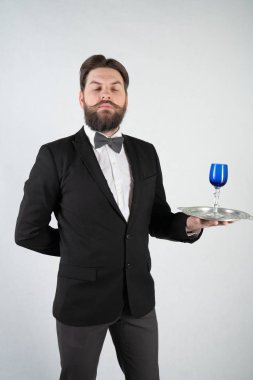 elini ve bir kadeh şarap beyaz sağlam bir arka plan stüdyo üzerinde çelik bir tepsi ile resmi iş takım elbiseli sakallı beyaz hizmetçi duruyor