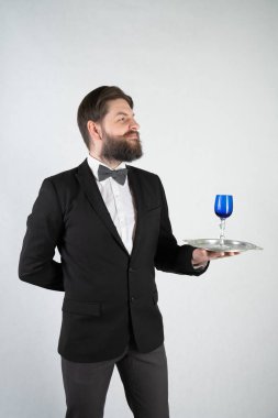 elini ve bir kadeh şarap beyaz sağlam bir arka plan stüdyo üzerinde çelik bir tepsi ile resmi iş takım elbiseli sakallı beyaz hizmetçi duruyor