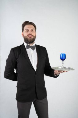 elini ve bir kadeh şarap beyaz sağlam bir arka plan stüdyo üzerinde çelik bir tepsi ile resmi iş takım elbiseli sakallı beyaz hizmetçi duruyor