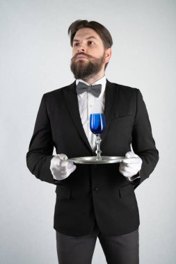 elini ve bir kadeh şarap beyaz sağlam bir arka plan stüdyo üzerinde çelik bir tepsi ile resmi iş takım elbiseli sakallı beyaz hizmetçi duruyor