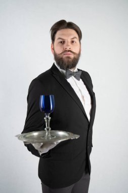 elini ve bir kadeh şarap beyaz sağlam bir arka plan stüdyo üzerinde çelik bir tepsi ile resmi iş takım elbiseli sakallı beyaz hizmetçi duruyor