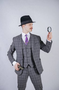 Beyaz katı Studio zemin üzerine bir büyüteç ve silah tutan adam bir kravat, bir iş ekose takım elbise giymiş bıyıklı