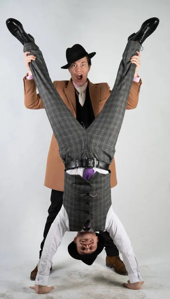 two friends dressed in vintage clothes in classic style and stand upside down and fool around on a white background