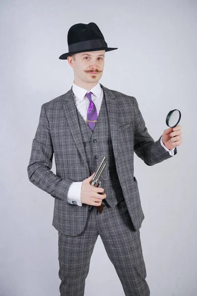 穿着商务格子西服 系领带的男子 拿着放大镜和枪 背景是白色的实木 Studio — 图库照片