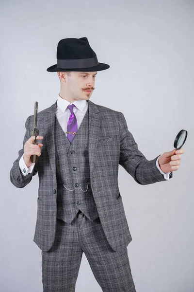 白色固体のスタジオ背景に虫眼鏡と銃を保持するいるとの提携で格子縞の背広に身を包んだ口髭の男 — ストック写真