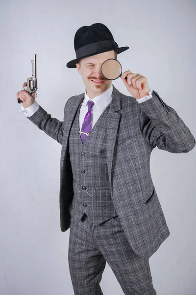 白色固体のスタジオ背景に虫眼鏡と銃を保持するいるとの提携で格子縞の背広に身を包んだ口髭の男 — ストック写真