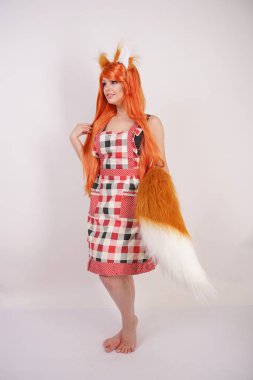 Tüylü büyük kulakları ile turuncu uzun peruk ve uzun kabarık kuyruk kırmızı mutfak ekose apron giyen beyaz bir arka planda yalnız yalınayak poz büyüleyici Fox kız