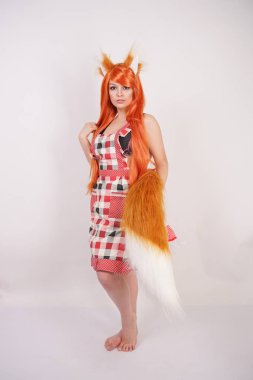 Tüylü büyük kulakları ile turuncu uzun peruk ve uzun kabarık kuyruk kırmızı mutfak ekose apron giyen beyaz bir arka planda yalnız yalınayak poz büyüleyici Fox kız