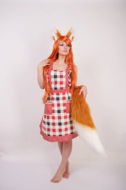 Tüylü büyük kulakları ile turuncu uzun peruk ve uzun kabarık kuyruk kırmızı mutfak ekose apron giyen beyaz bir arka planda yalnız yalınayak poz büyüleyici Fox kız