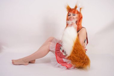 Tüylü büyük kulakları ile turuncu uzun peruk ve uzun kabarık kuyruk kırmızı mutfak ekose apron giyen beyaz bir arka planda yalnız yalınayak poz büyüleyici Fox kız