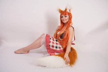 Tüylü büyük kulakları ile turuncu uzun peruk ve uzun kabarık kuyruk kırmızı mutfak ekose apron giyen beyaz bir arka planda yalnız yalınayak poz büyüleyici Fox kız
