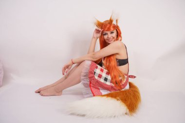 Tüylü büyük kulakları ile turuncu uzun peruk ve uzun kabarık kuyruk kırmızı mutfak ekose apron giyen beyaz bir arka planda yalnız yalınayak poz büyüleyici Fox kız