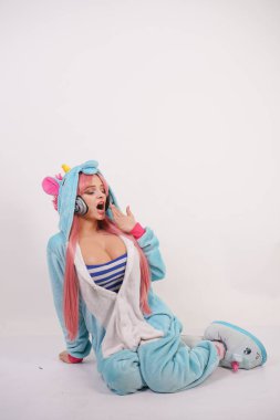 Mavi tek boynuzlu at pijama ve yumuşak komik terlik Studio beyaz arka plan üzerinde pembe uzun saçlı sevimli genç kız