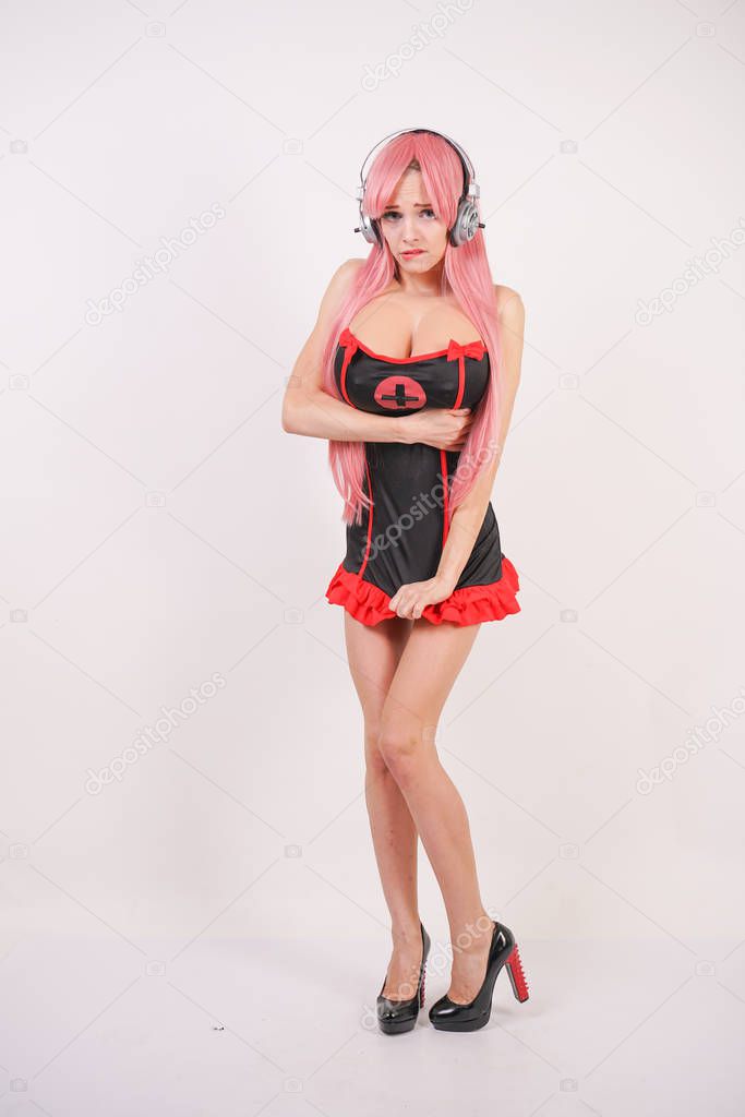 cute young girl with pink long hair in black with red sex nurse uniform with big boobs posing on white background in Studio