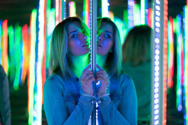 sweet caucasian girl walks in a mirror maze with colorful diodes and enjoys an unusual attraction room in the city