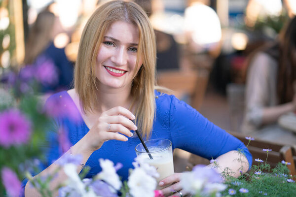 charming caucasian blonde girl in a blue dress sitting at a table in a city cafe alone and waiting