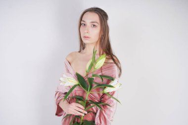 büyük gözleri ile utangaç beyaz kız kadife pembe elbise standları ve masum ve saflık sembolü olarak elinde beyaz bir zambak tutar. beyaz stüdyo arka planda poz genç kadın.