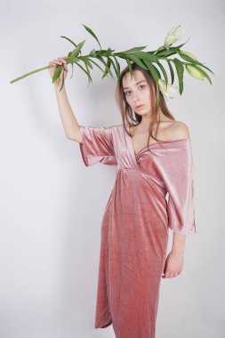 büyük gözleri ile utangaç beyaz kız kadife pembe elbise standları ve masum ve saflık sembolü olarak elinde beyaz bir zambak tutar. beyaz stüdyo arka planda poz genç kadın.